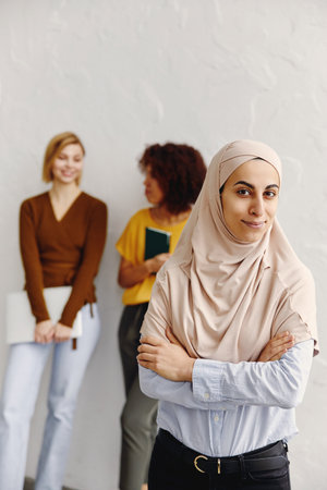 Beautiful arab businesswoman in hijab looking at camera and smiling with multiethnic colleagues in background.の写真素材