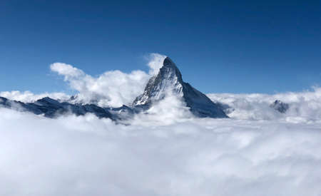 Perfect view of the Matterhorn in Zermatt at a perfect sunny day, with blue sky and perfect light. In the valley sea of clouds fog dust with matterhorn emerging from the clouds. The snowy Swiss mountains and landscape in winter is extraordinary. After a long skiing day these views are incredible.の写真素材