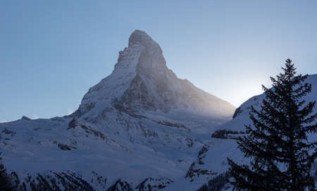 Perfect view of the Matterhorn in Zermatt at sunset with backlight and the sun behind the mountain. The snowy Swiss mountains and landscape in winter is extraordinary. After a long skiing day these views are incredible.の写真素材