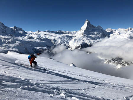 Single person skier skiing in front of the matterhorn and blue sky on a sunny day. After skiing...