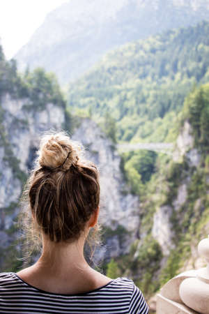 A Person lonely female brown haired looking from Neuschwanstein castle over to the Marien bridge and the valley beneath it, the Tegelberg in the background. Bad weather mood.の写真素材