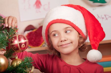 little girl in the hat of Santa Claus decorates a Christmas treeの写真素材