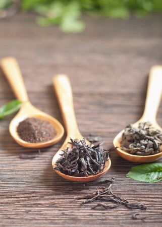 Different kinds of green and black dry tea in  spoon against a wooden tableの写真素材