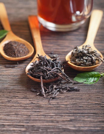 Different kinds of green and black dry tea in  spoon against a wooden tableの写真素材