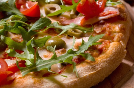 Sliced pizza with arugula and cherry tomatoes on wooden boardの写真素材