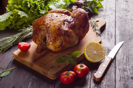 Whole roasted chicken with vegetables, on wooden tableの写真素材