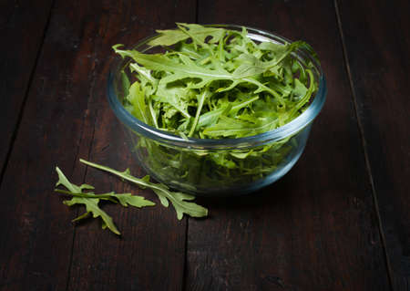 Fresh arugula in a plate on rustic wooden background