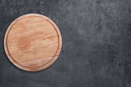Rustic wooden round cutting board on black stoneの写真素材