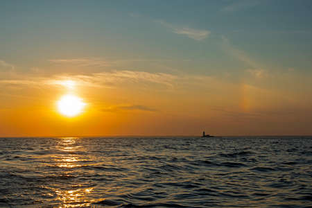 Sunset over the waters of the Bay with a sun halo and the silhouette of the lighthouseの写真素材