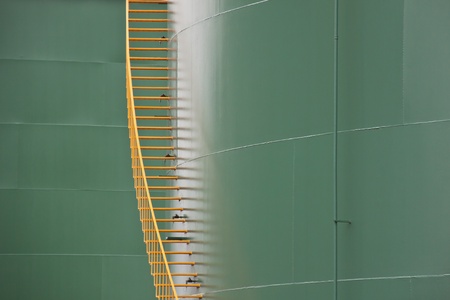 Vertical yellow metal stairs between two huge green gas tanks の写真素材