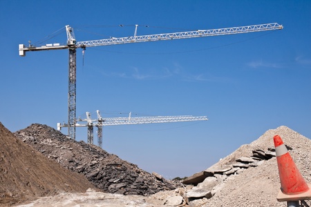 Tree white cranes against a blue sky on a construction site with some mountains of broken concreteの写真素材