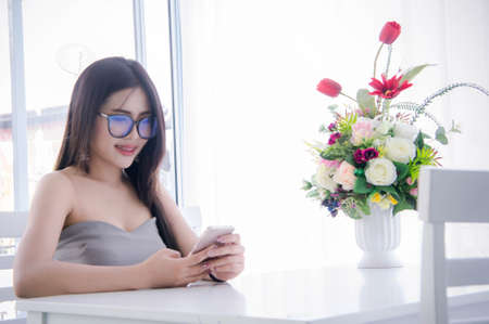 Girl's looking and enjoy smartphone in her hand and laugh sitting on chair in the roomの写真素材