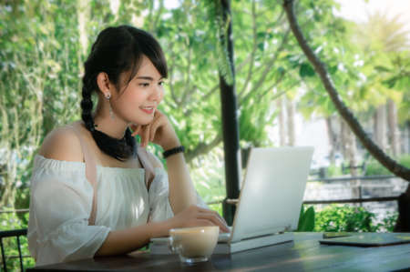asian girl's sitting and using laptop looking smile on work in the cafeの写真素材