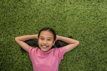 kid asian girl's lie leisurely on the Lawn floor and smile looking atの写真素材