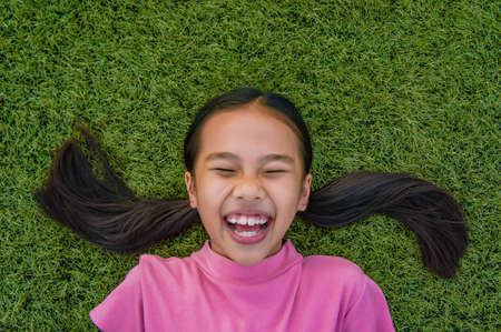 kid asian girl's lie leisurely on the Lawn floor and smile looking at
