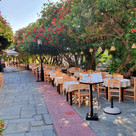 Kos, Greece - September 17, 2019: Typical small Greek atmospheric restaurants in the middle of the city. Colorful chairs and tables outside.のeditorial素材