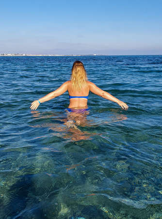 A woman with blonde hair enters the turquoise water in a bathing suitの写真素材