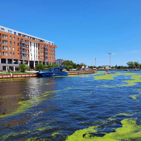 Gdansk, Poland - July 11, 2021: View of the old city of Gdansk on the Motlawa River. Tourists walk along the waterfront. On Motlawa green patches of duckweed. Middle of the river flows ship.のeditorial素材