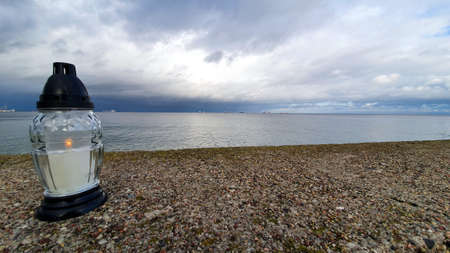 A lit white candle by the sea. Symbol of remembrance of the victims at sea.