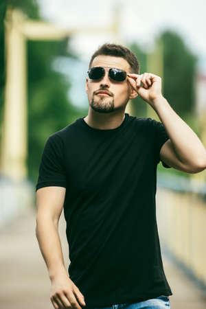 The guy with glasses on the street. Portrait of a young guy. Man on the nature in the summer. Walks...