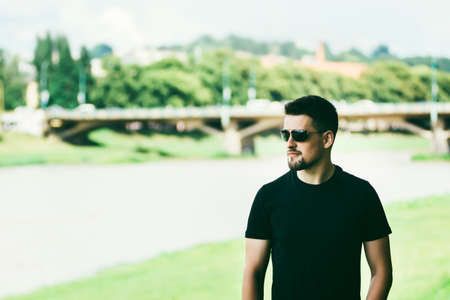 The guy with glasses on the street. Portrait of a young guy. Man on the nature in the summer. Walks...
