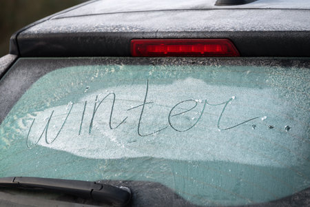 The description "winter" on the rear window of the car. The black car is covered with snow and a crust of ice. Winter, danger, safety, insurance, winter tires. Cold weather outside. Black, white, blueの写真素材
