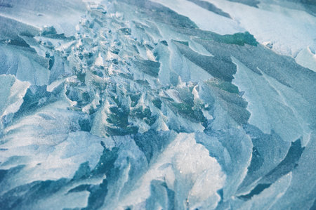 A close-up of ice texture partially covered with snow. The surface displays intricate frozen...