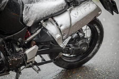 A large black touring motorcycle is covered in snow. The end of the motorcycle season, winter.