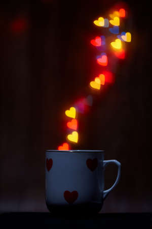 Cup emits steam of glowing hearts on dark background with copy spaceの写真素材