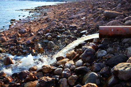 Bank of the river with large boulders and the water flows from the sewer pipe in spring dayの写真素材