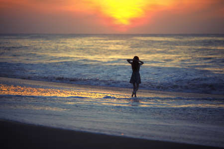 Girl watching the sunrise over the ocean with his hands behind her headの写真素材