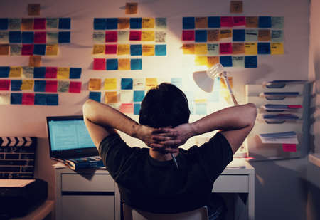 man sitting in front of computer with switched on table lamp and sticky notes on the backgroundの写真素材