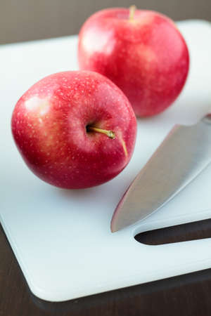 Two red apples and a knife on a white cutting boardの写真素材