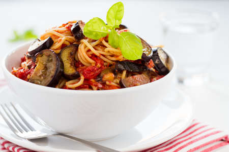 Spaghetti with eggplants and tomatoes served on a white plateの写真素材