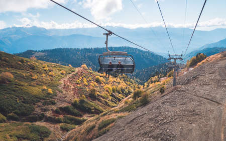 KRASNAYA POLYANA, SOCHI, RUSSIA - OCTOBER 13, 2017: Tourists in chair lift (funicular) observing magnificent scenery with mountain ridges in blue haze in backgroundのeditorial素材