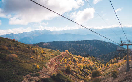 Chair lift (funicular) with unidentified people observing amazing scenery with mountain ridges and autumn forests in background. Krasnaya Polyana, Sochi, Russiaの写真素材