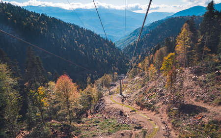 Chair lift (funicular) moving amidst magnificent autumn forests and mountain slopes with mountain ridges in blue haze in background. Krasnaya Polyana, Sochi, Russiaの写真素材