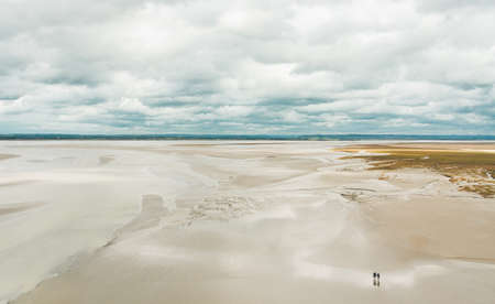 Unidentified people walking on sands during low tide outside Le Mont Saint-Michel tidal island in Normandy, Franceの写真素材