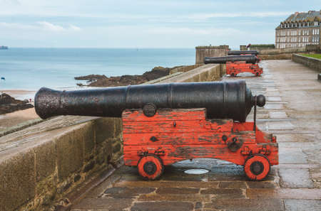 Old aged cannons on red wooden carriages facing the sea on ancient fortification ramparts of Saint-Malo, Brittany, Franceの写真素材