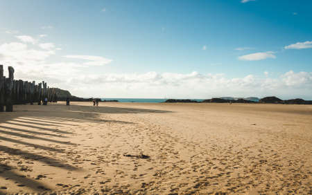 Wooden poles casting shadows on sandy beach on bright sunny day in Saint-Malo, Brittany, Franceの写真素材