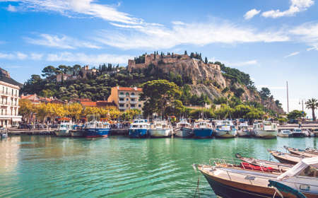 Boats moored in harbour with Chateau de Cassis atop a hill in background on bright sunny day in Cassis, Franceの写真素材