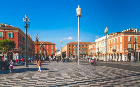 NICE, FRANCE - OCTOBER 11, 2009: Red ochre buildings of Italian architecture on Place Massena in Nice, historic square with statues created by Jaume Plensaのeditorial素材