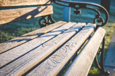 Wooden bench with forged cast iron handles and planks covered with sparkling hoar frost. Shallow depth of field. For wallpaper, backgroundの写真素材