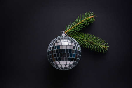 Big bauble made of mirror pieces decorated with spruce twigs against black background