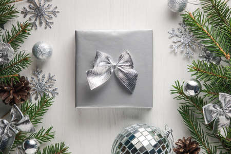 Christmas present wrapped in silver paper decorated with shining bow on white background surrounded...