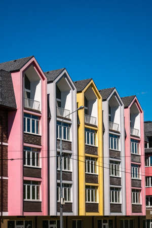 Rows of triangular elements of roofline covered with shingle, with chimney against blue sky. Colorful pink and yellow house. Vertical shotの写真素材