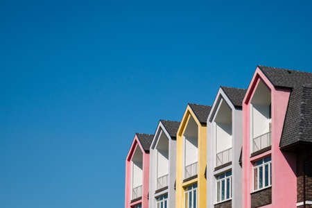 Rows of triangular elements of roofline covered with shingle, colorful pink and yellow house against blue sky. Copy spaceの写真素材