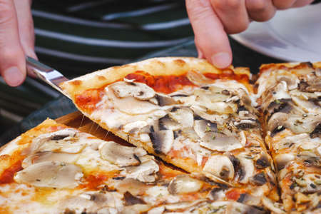 Female hands taking slice of freshly baked thin mushroom pizza in restaurant