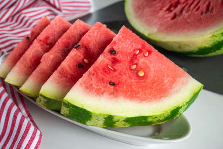 Triangular slices of ripe watermelon with red flesh served on white plate