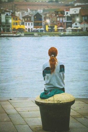 A young girl sits waiting on the river embankmentの写真素材